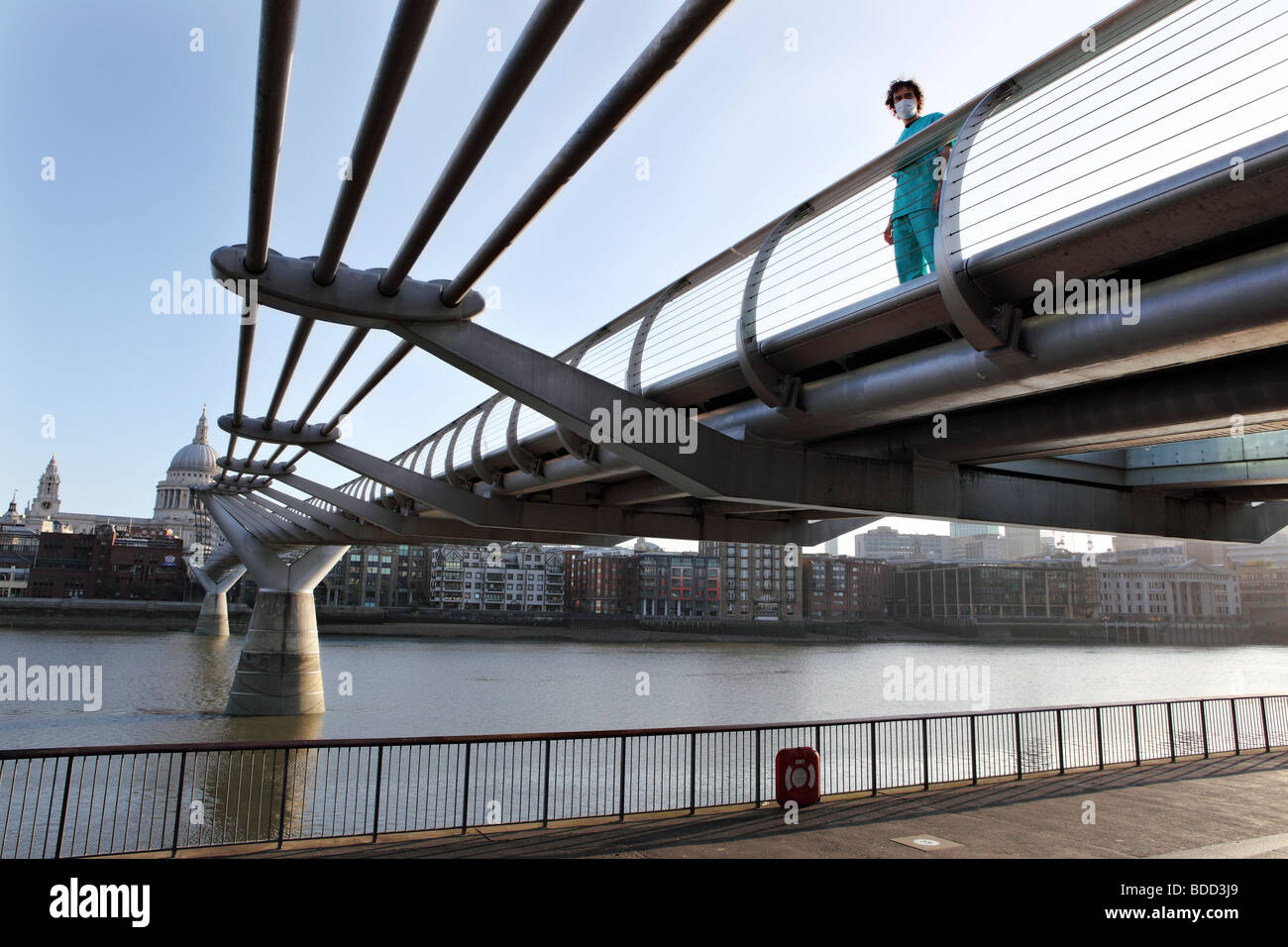 Un jeune homme avec un masque chirurgical et médical est encore aujourd'hui uniforme sur la passerelle du Millenium, à Londres. Banque D'Images