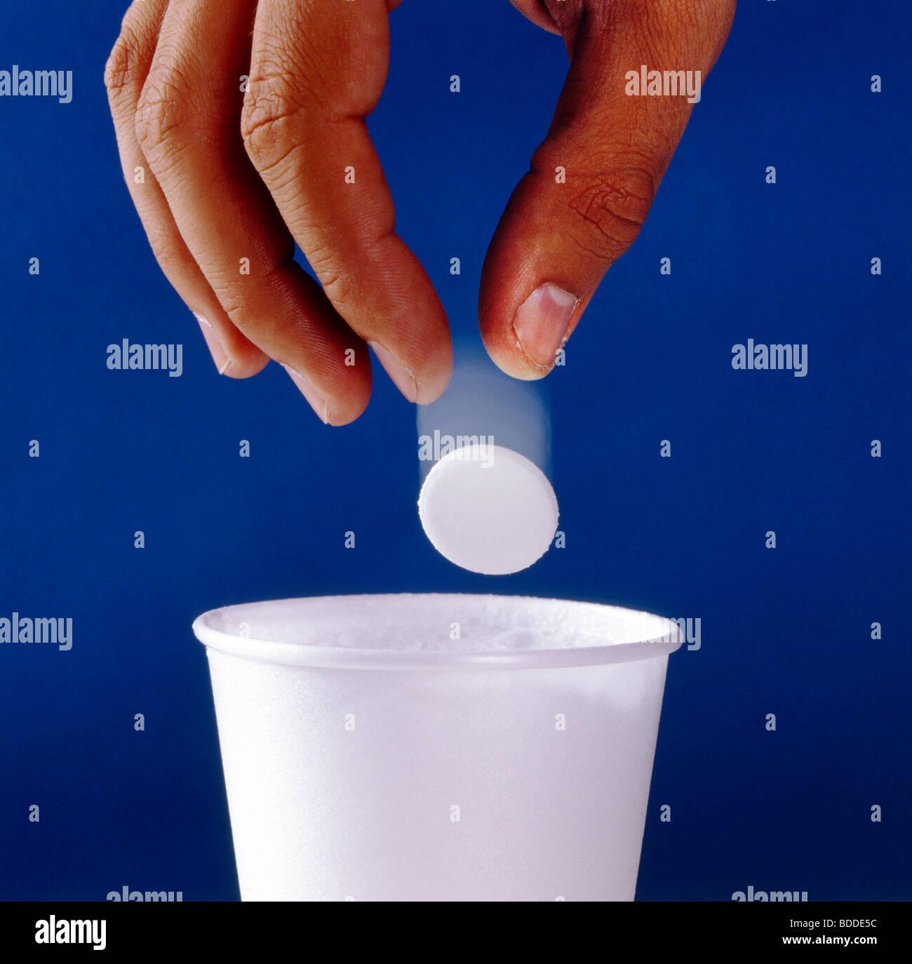 Close up de la main d'un homme laissant tomber un ALKA SELTZER (antiacides et le soulagement de la douleur médecine) dans une tasse d'eau. Banque D'Images