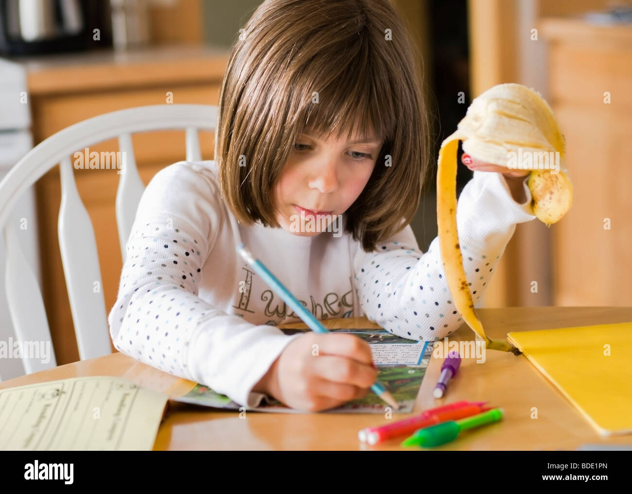 Une jeune fille mange une collation santé et fait ses devoirs après l'école. Banque D'Images