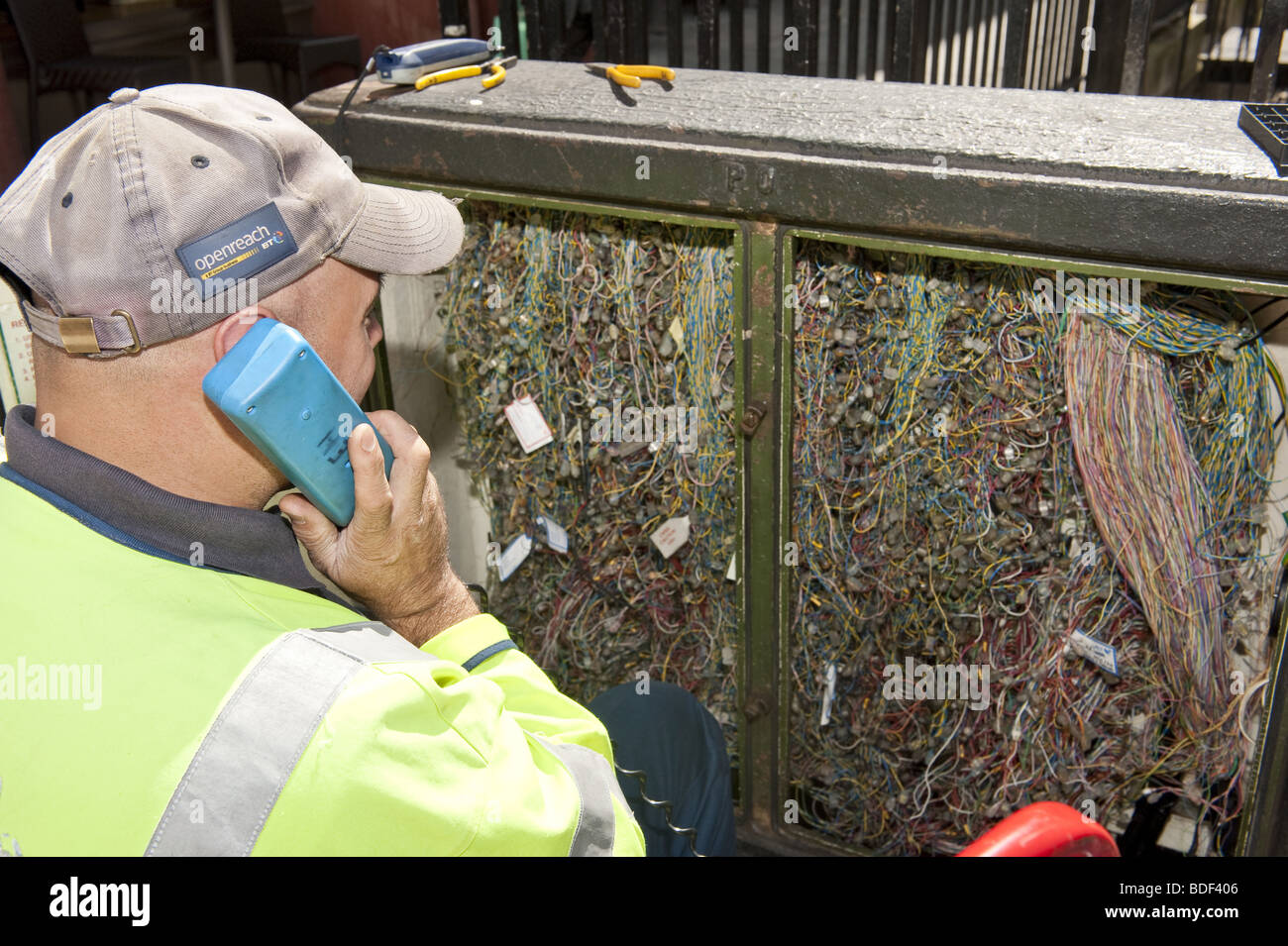 Regarder par-dessus l'épaule de l'ingénieur télécommunications BT sur le téléphone en face d'ouvrir le boîtier de raccordement sur la rue Banque D'Images