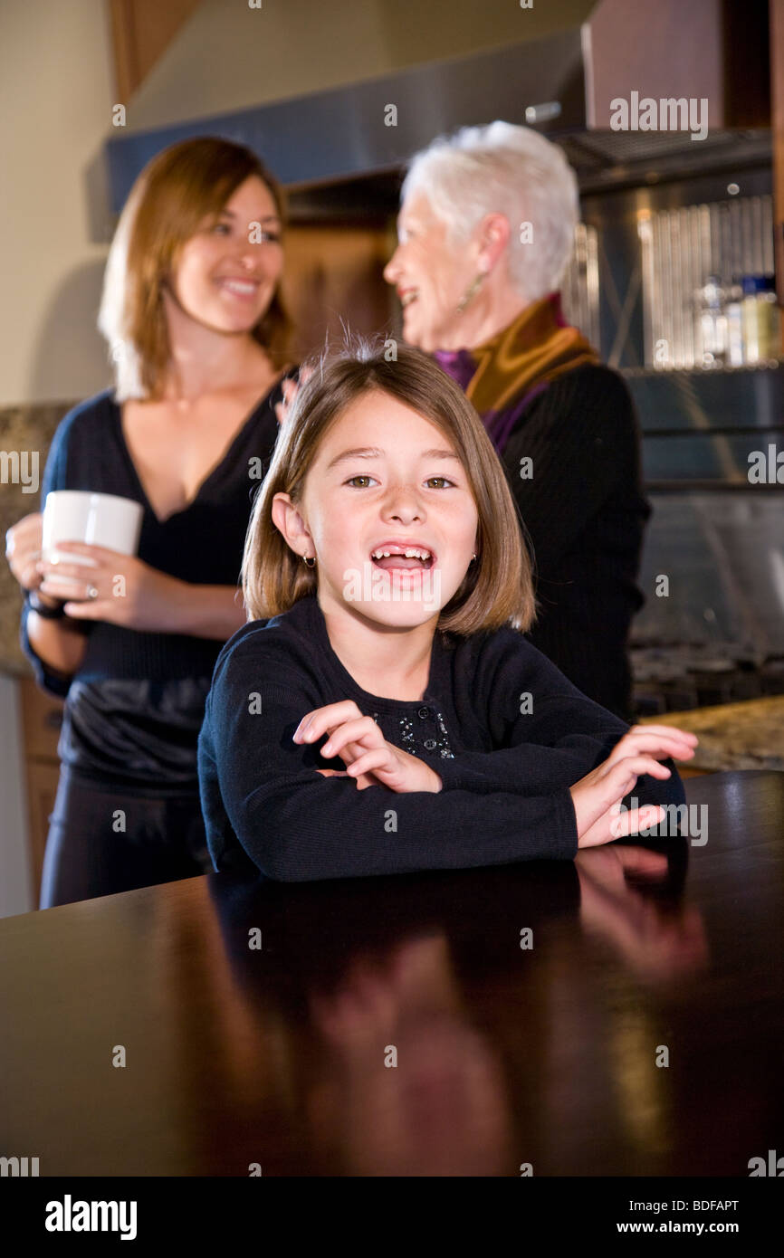 Fille Assise Dans La Cuisine Avec Maman Et Grand Mère En Arrière Plan Photo Stock Alamy 