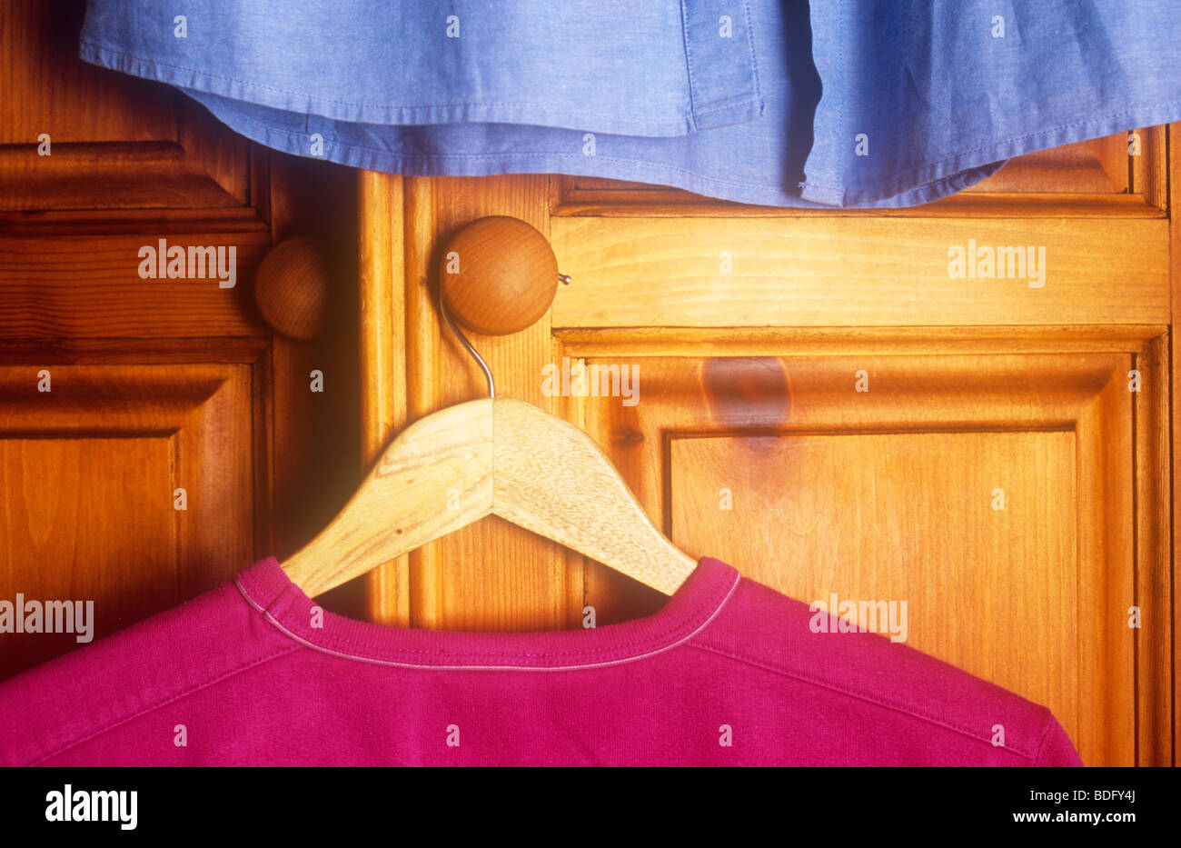Sweat rouge sur cintre en bois bois de pin de poignée armoire avec chemise bleue au-dessus Banque D'Images Sweat rouge sur cintre en bois bois de pin de poignée armoire avec chemise bleue au-dessus Banque D'Images