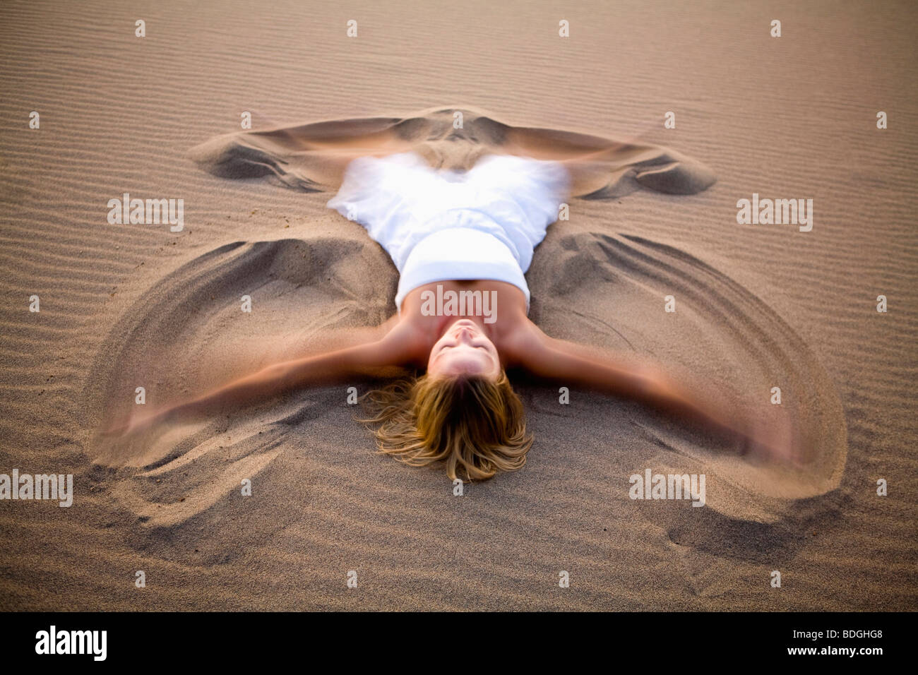 Une femme en blanc faisant un ange de sable sur les Dunes de Stovepipe Wells dans la vallée de la mort, en Californie. Banque D'Images