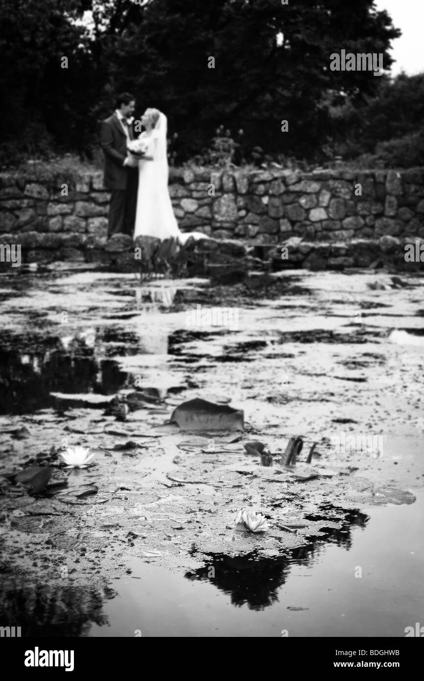 Lily sur l'étang avec des époux et l'épouse n'est pas mise au point en arrière-plan sur la marche de jour de mariage dans les jardins à réception de mariage Banque D'Images