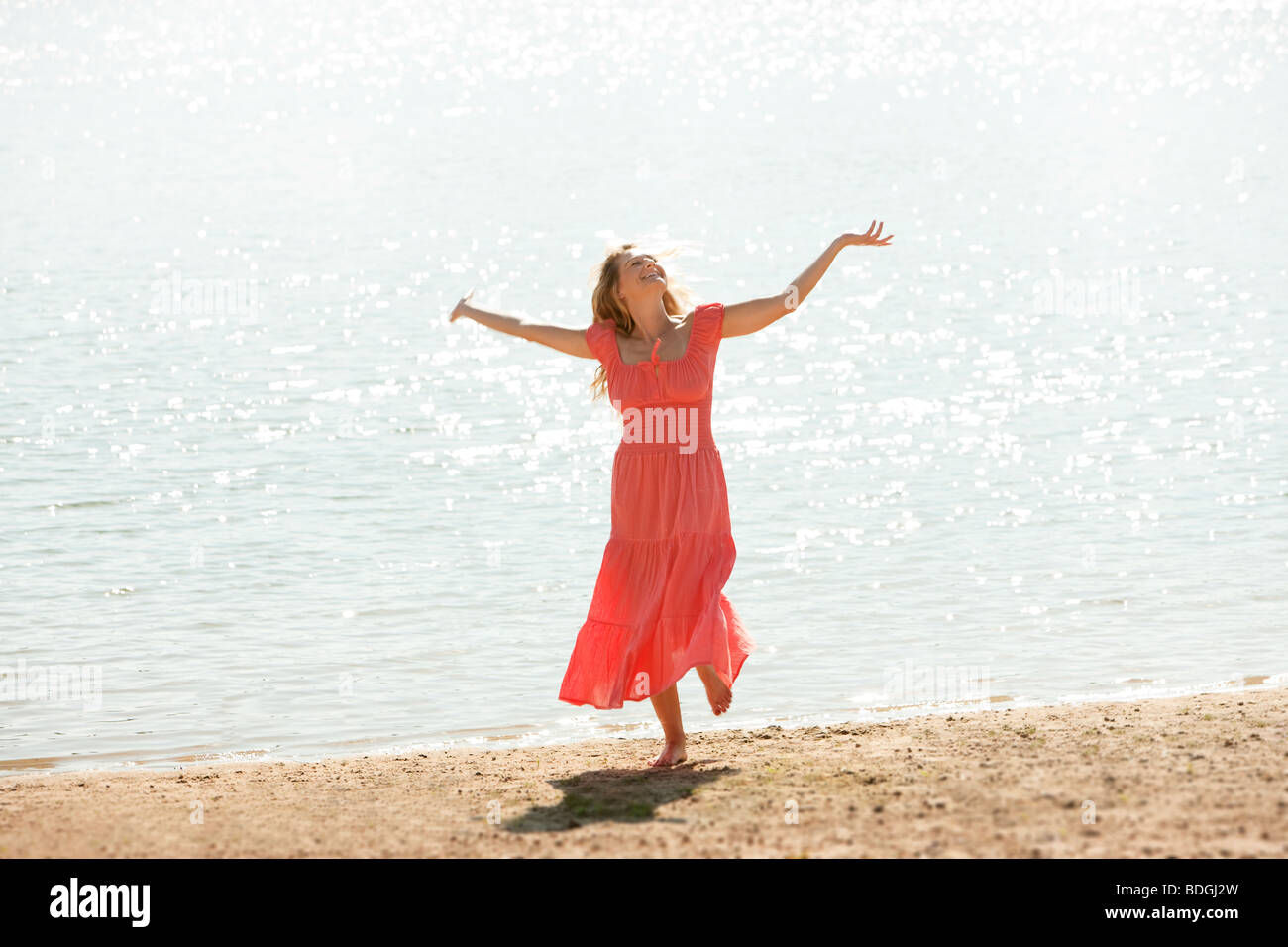 Un heureux , smiling woman danse sur une plage avec l'abandon, les bras tendus. Banque D'Images