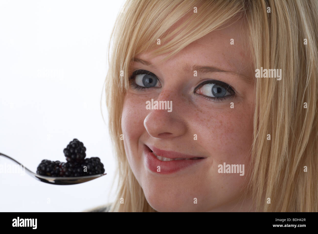 Jeune femme blonde de 20 ans avec une cuillerée de mûres fraîches avec un sourire heureux Banque D'Images