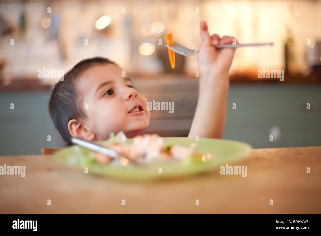 Garçon jouant avec sa nourriture sur une fourchette à une table de cuisine Banque D'Images