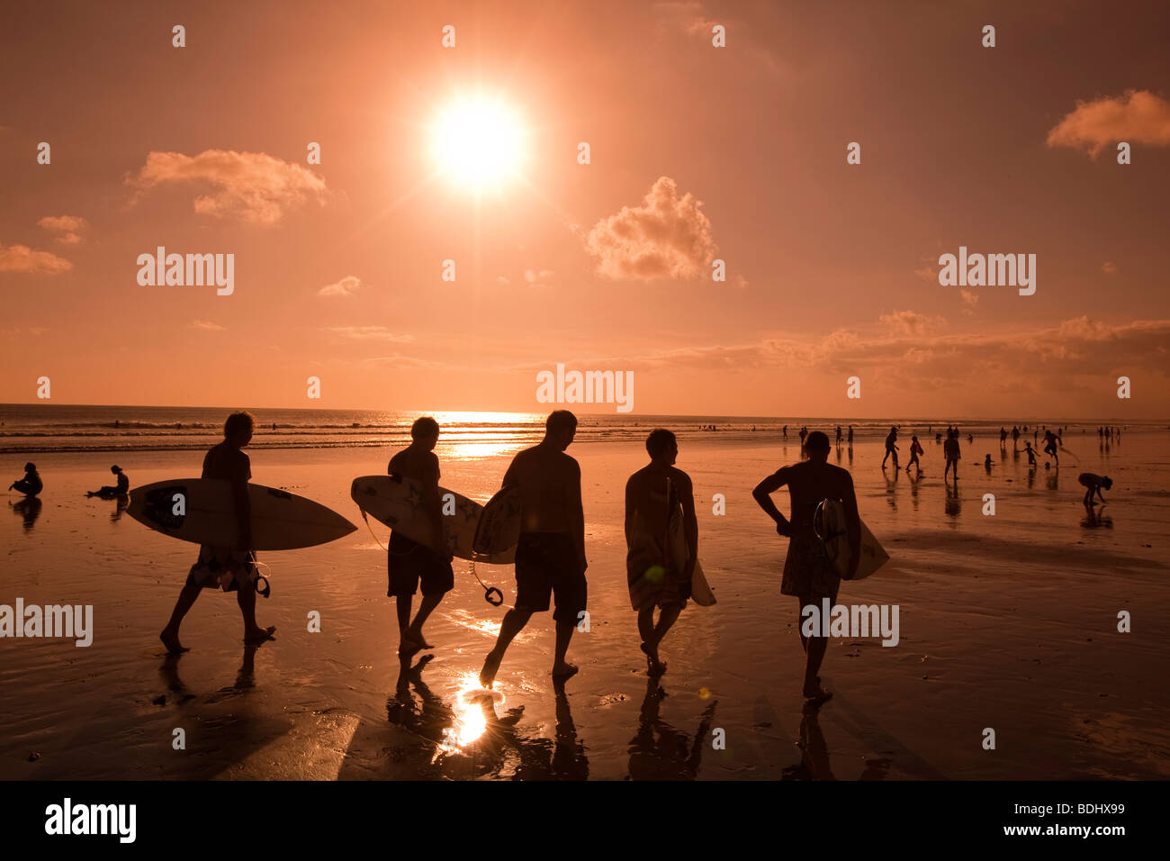 L'INDONÉSIE, Bali, Kuta, plage, groupe d'internautes masculins au coucher du soleil à marcher le long du sable mouillé à la fin de jours de surf Banque D'Images