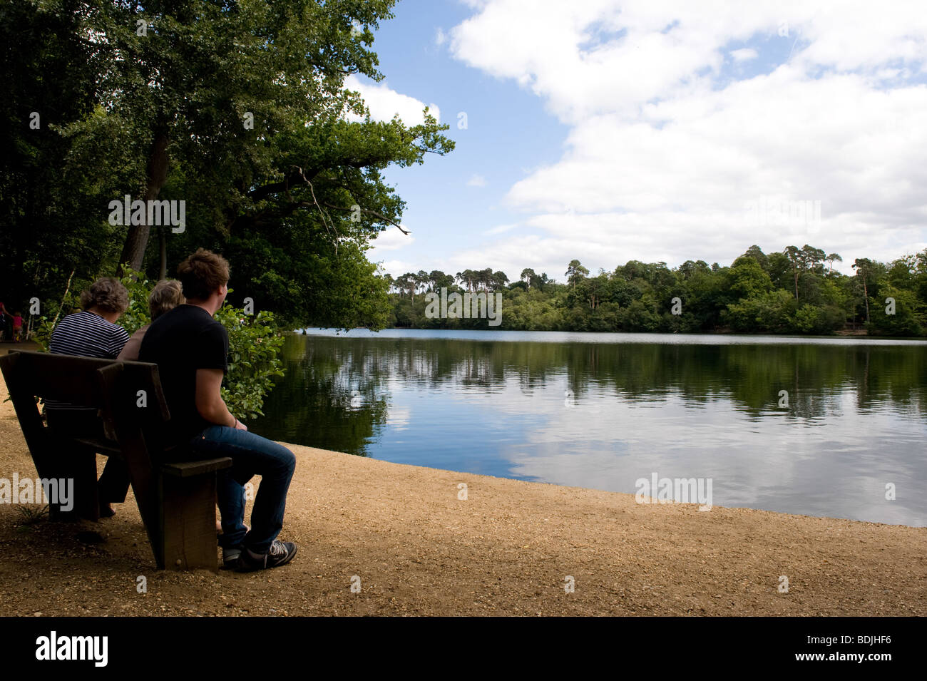 Trois personnes à s'assit sur un banc au bord du lac à Black Park Country Park, Buckinghamshire, Angleterre Banque D'Images