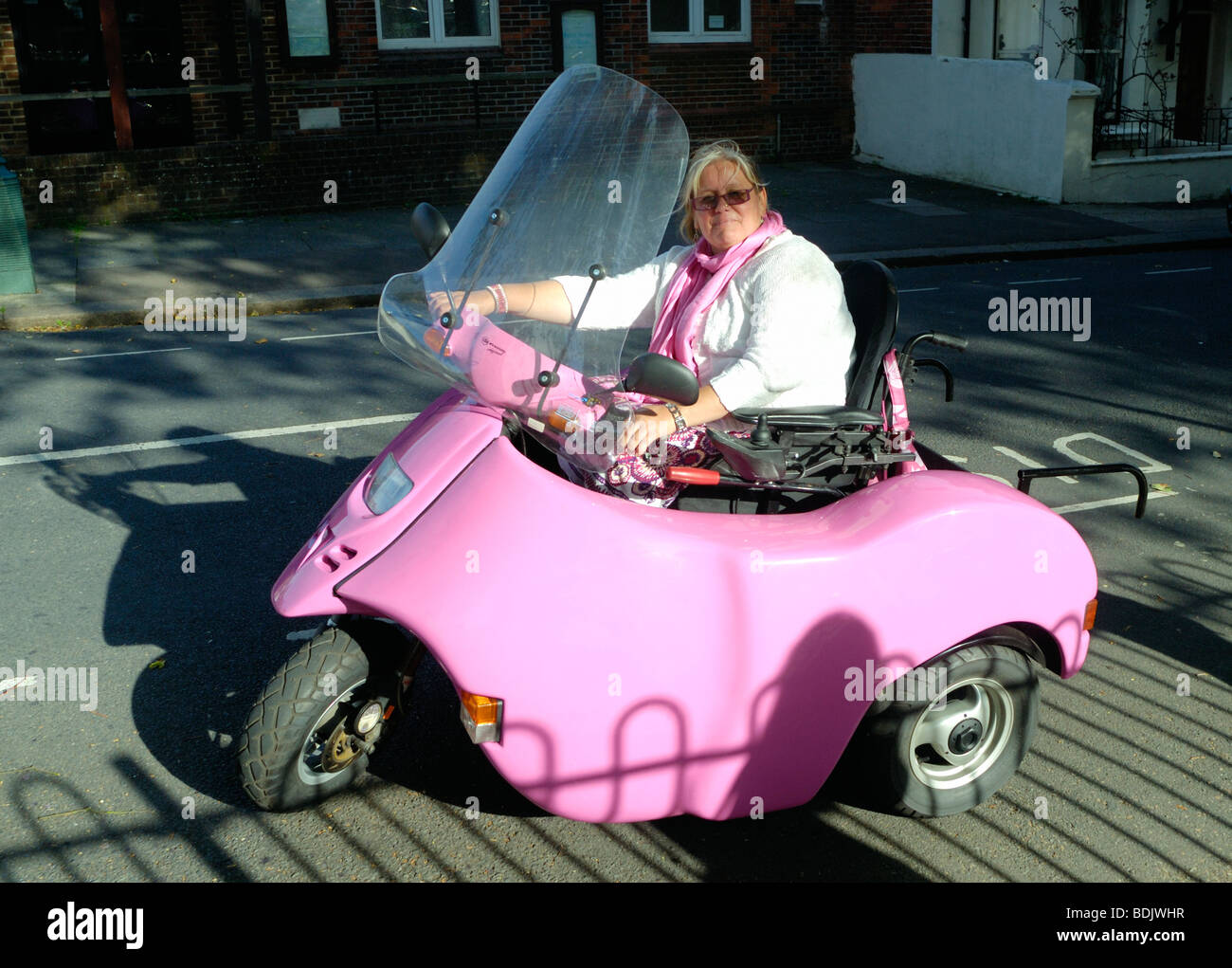 Une dame conduisant un scooter handicap rose Banque D'Images