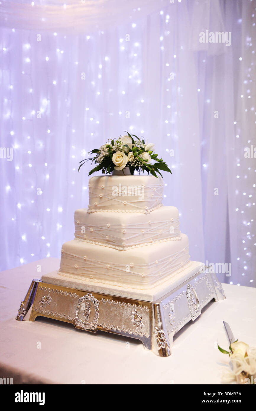 Gâteau de mariage blanc à trois niveaux d'argent orné sur le stand avec cake knife et pourpre à l'arrière-plan de décoration réception de mariage Banque D'Images