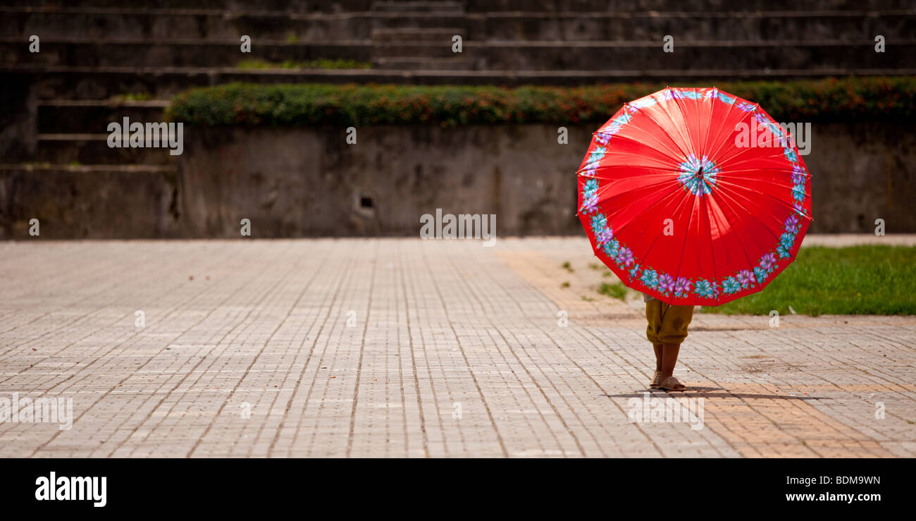 Un enfant joue avec un parapluie rouge vif dans le parc Banque D'Images