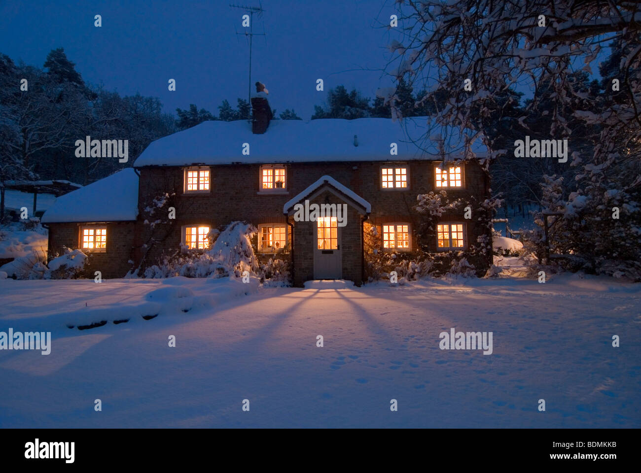 Carte de Noël scène de chalet confortable au crépuscule dans la neige vierge avec lumière fanning out à partir de windows Banque D'Images