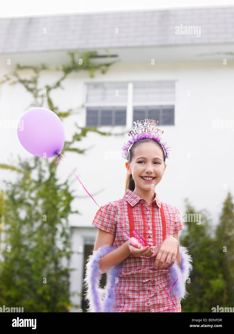 Girl (10-12) en plume boa holding balloon outside house Banque D'Images