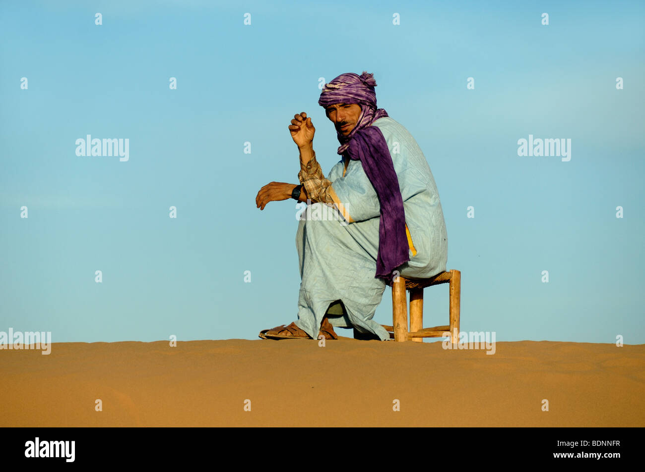 Homme berbère ou tribu portant des robes bleues traditionnelles, des vêtements, des vêtements ethniques ou une robe ethnique est assis sur un tabouret dans le désert du Sahara, près de Zagora, Maroc Banque D'Images