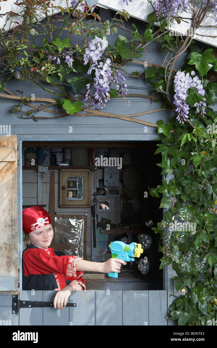 Jeune garçon (7-9) en costume pirate visant avec arme-jouet de shed Banque D'Images