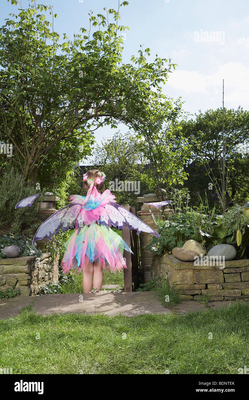 Jeune fille (5-6) wearing costume fée debout dans jardin, vue arrière Banque D'Images