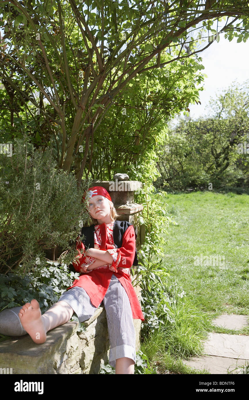 Young boy (7-9) wearing pirate costume assis les bras croisés en jardin Banque D'Images