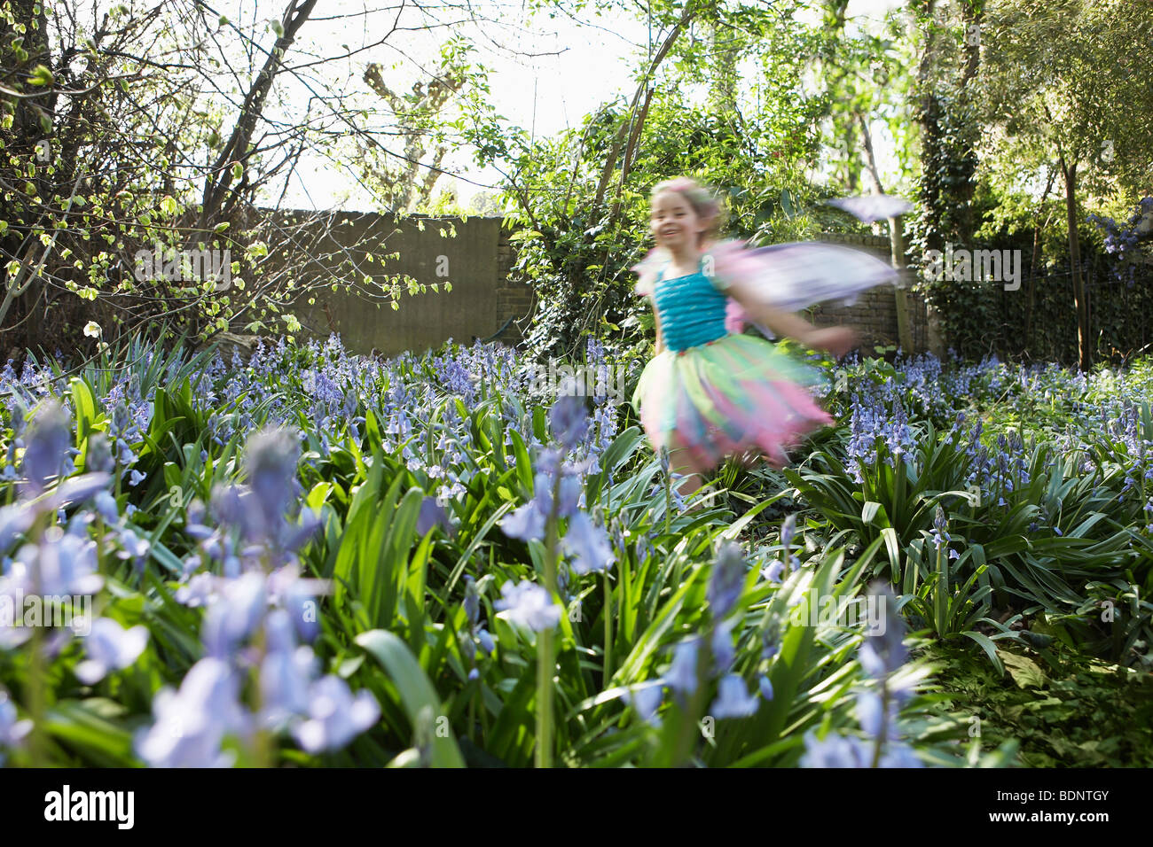 Jeune fille (5-6) s'exécutant dans le jardin de fleurs portant des costumes de fées, motion blur Banque D'Images