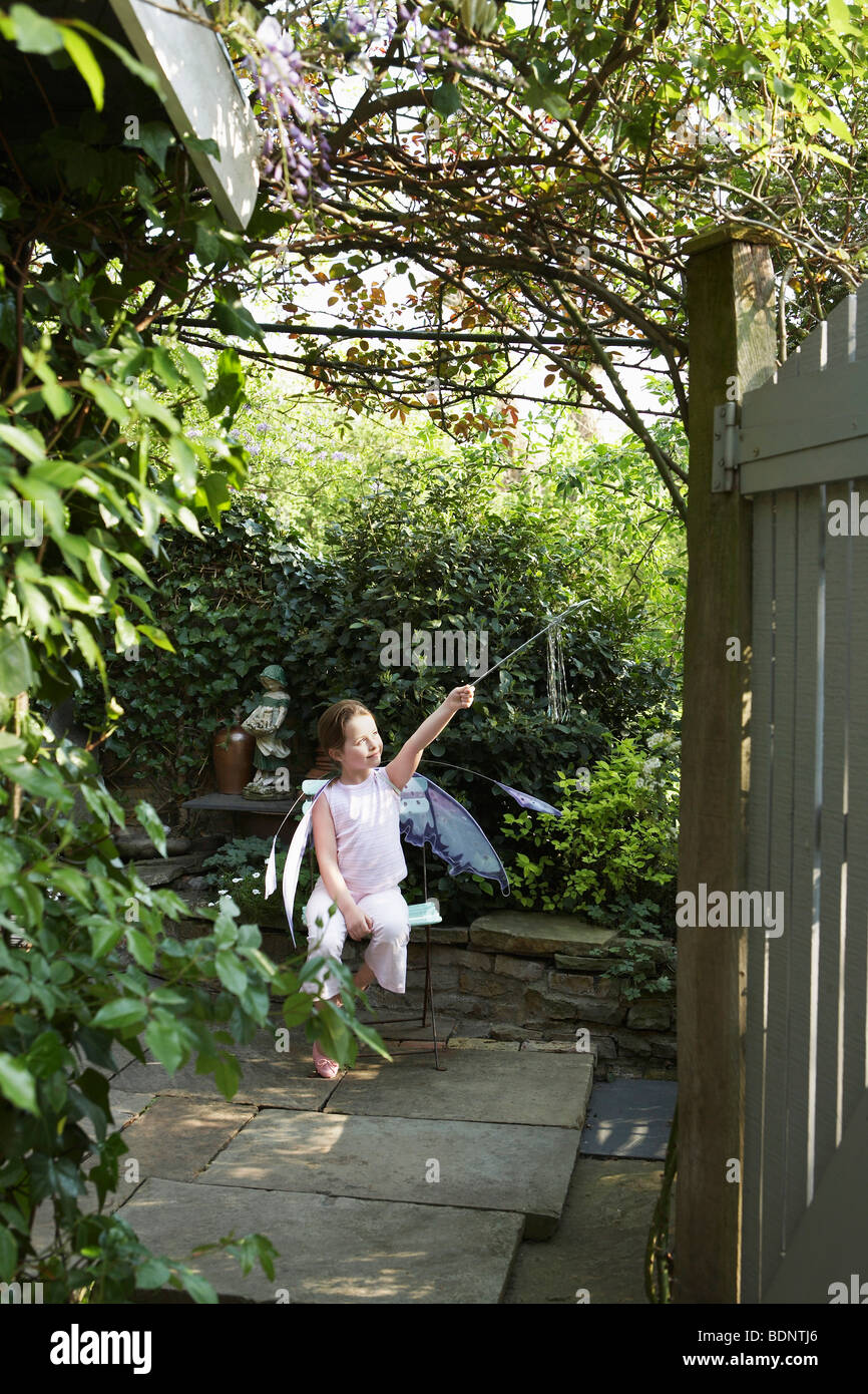 Jeune fille (5-6) sitting in garden in fairy costume holding baguette magique Banque D'Images