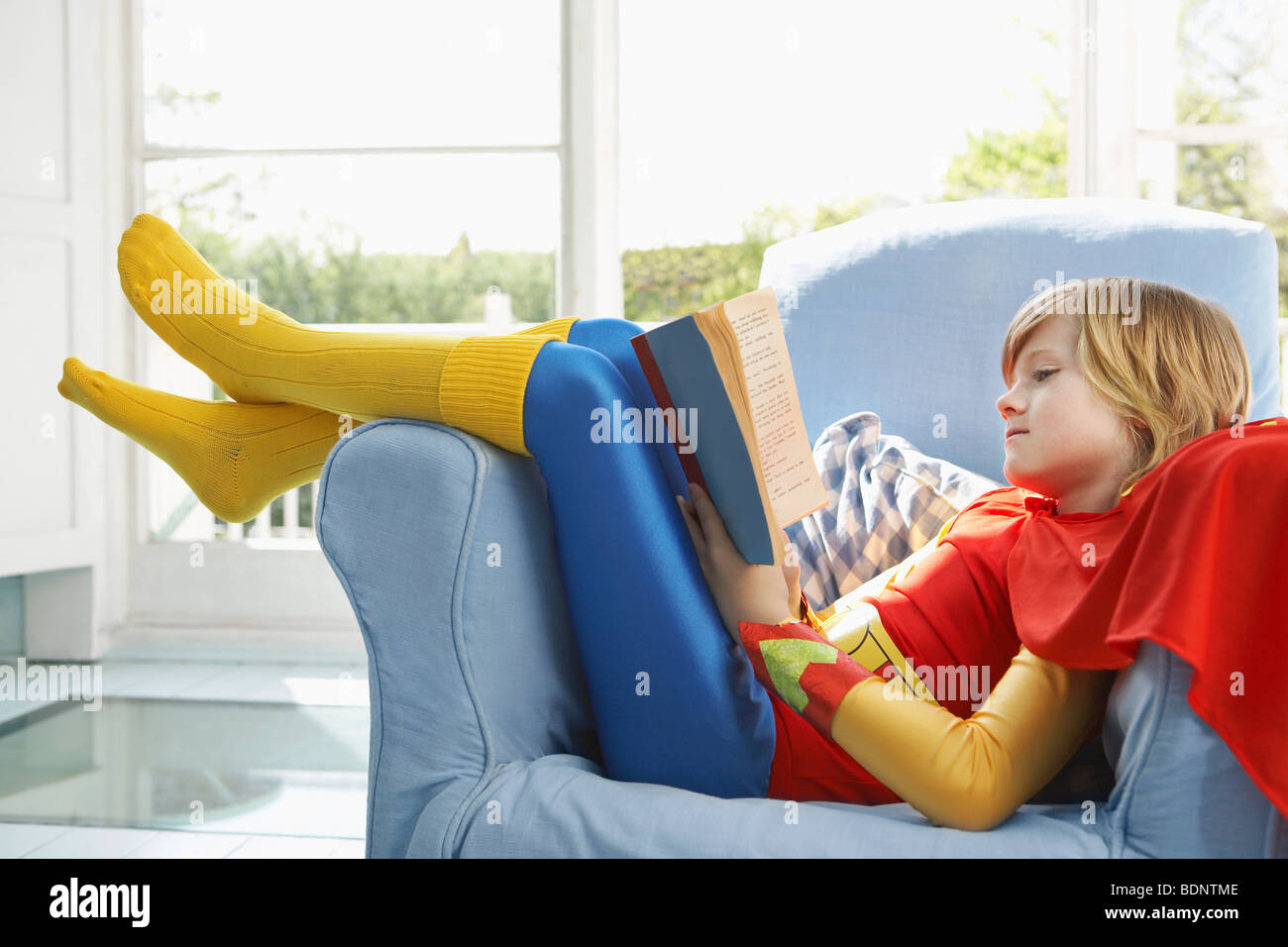 Young boy (7-9) sitting in armchair lecture, wearing superhero costume, side view Banque D'Images
