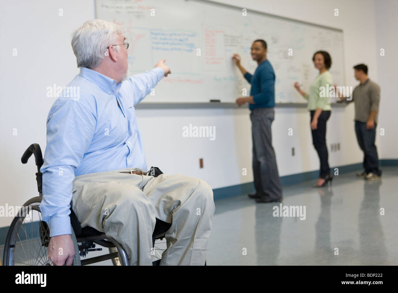 Professeur d'université dans un fauteuil roulant en montrant ses élèves écrivant sur un tableau. Banque D'Images