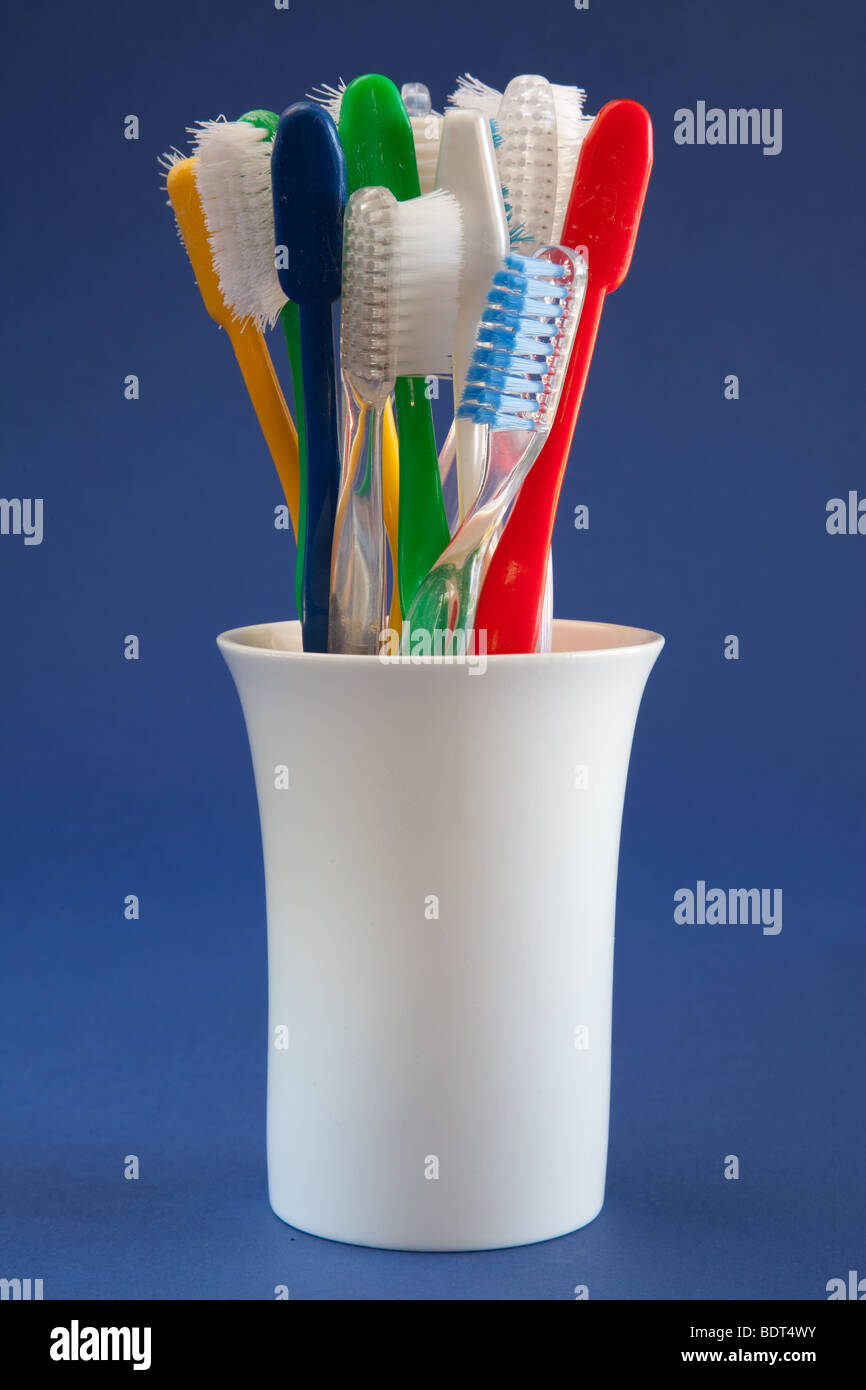 Vieille brosse à dents de couleurs variées dans un contenant en céramique blanche avec un fond bleu Banque D'Images