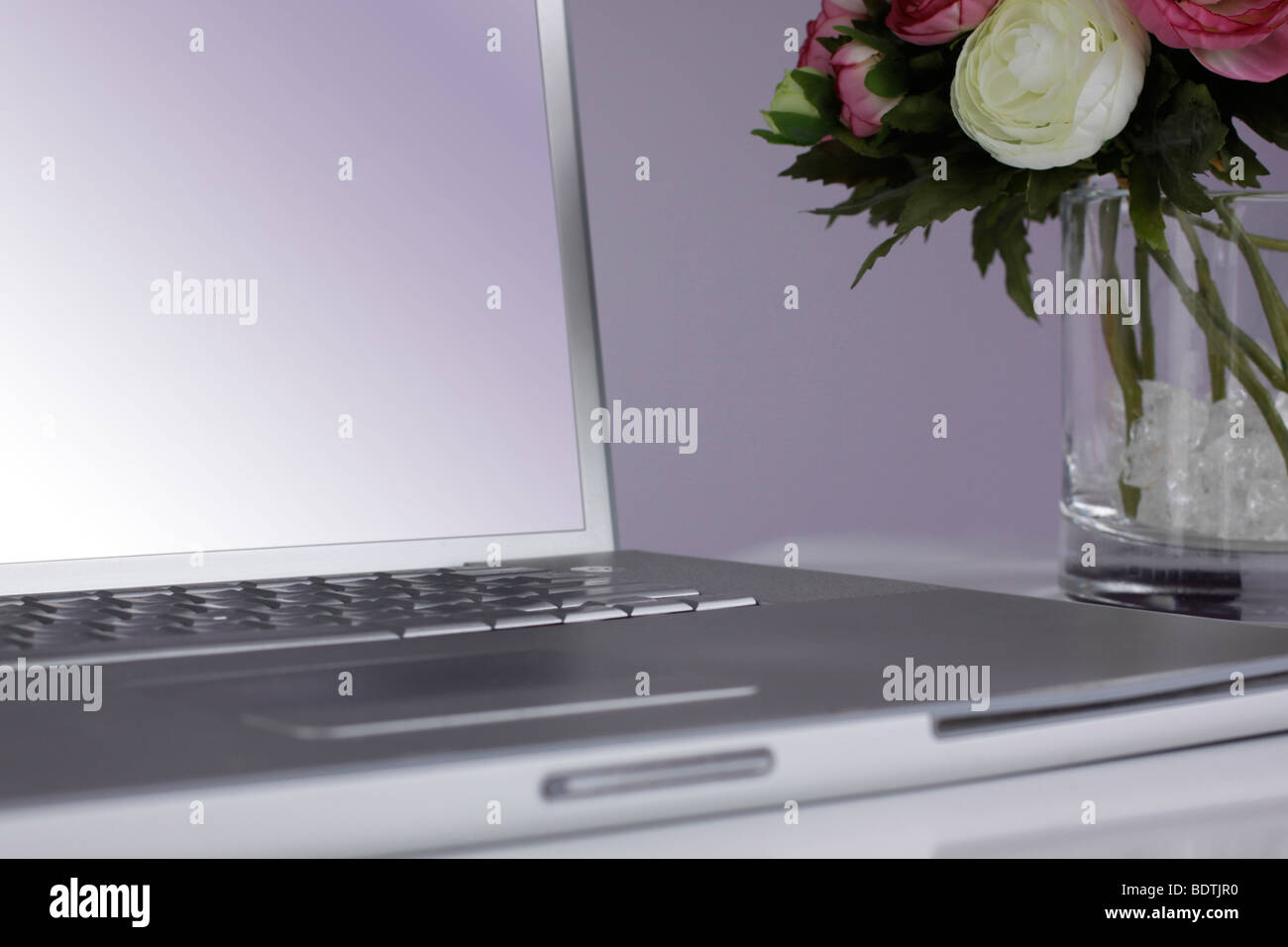 Ordinateur portable d'argent sur un bureau avec un vase blanc avec de belles fleurs roses et blanches à côté. Banque D'Images