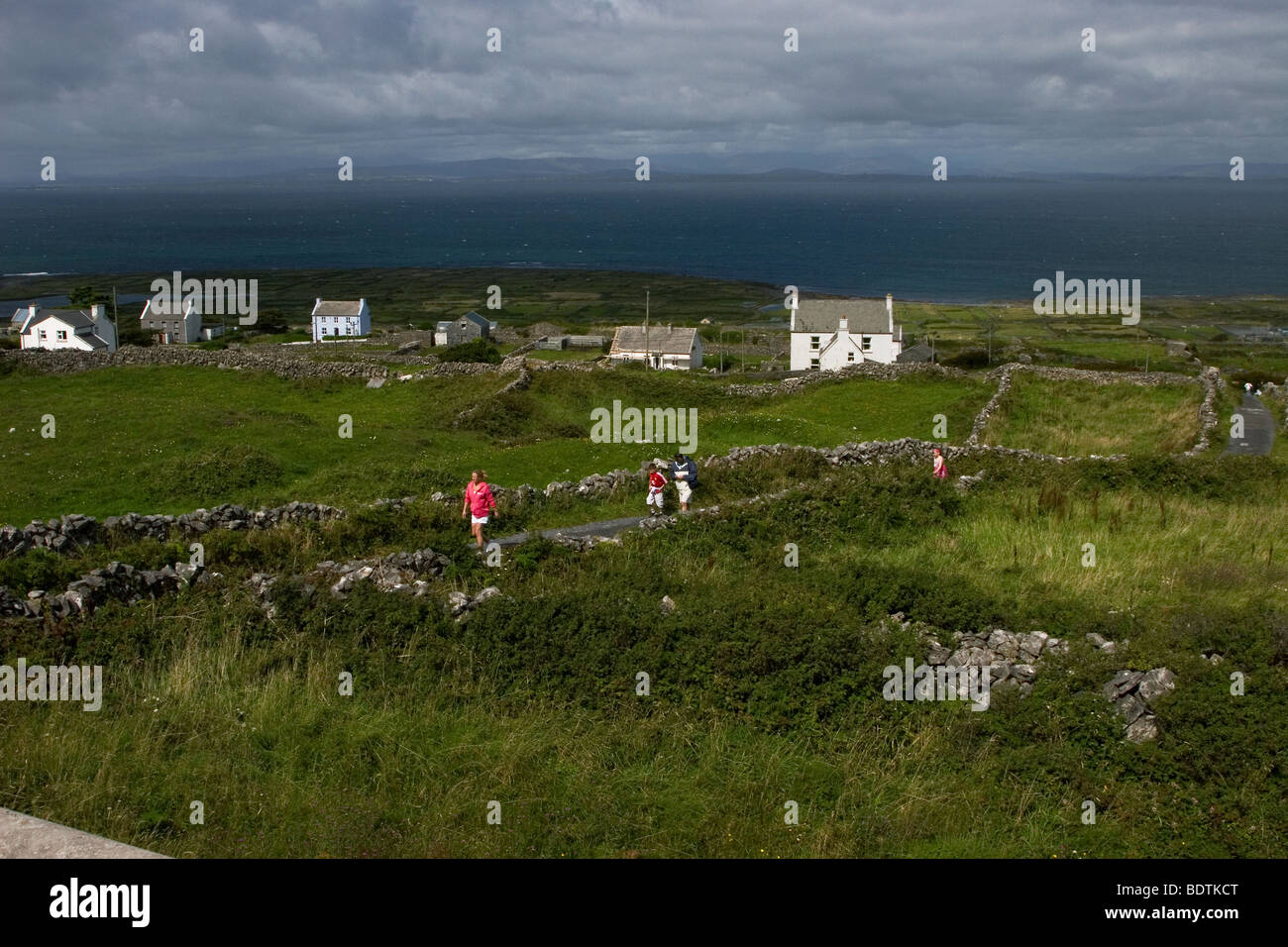 Les touristes à pied sur des routes de campagne bordée de Stonewall de Inis Mor (Inismore) Island, Îles d'Aran, dans le comté de Galway, Irlande. Banque D'Images