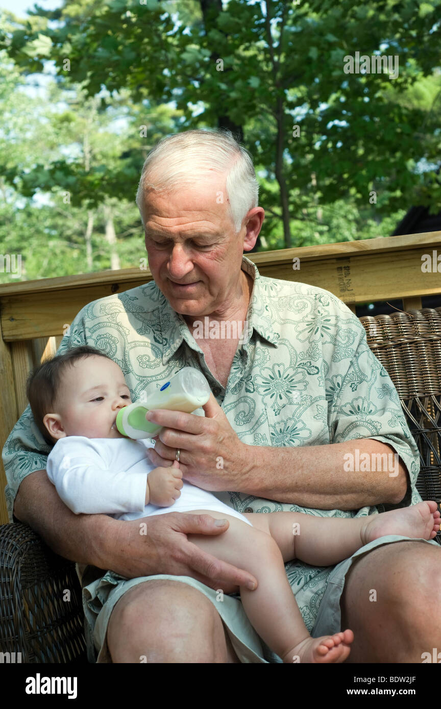 Grand-père nourrit ses petit-fils de 8 mois sur le porche de sa maison d'été Banque D'Images