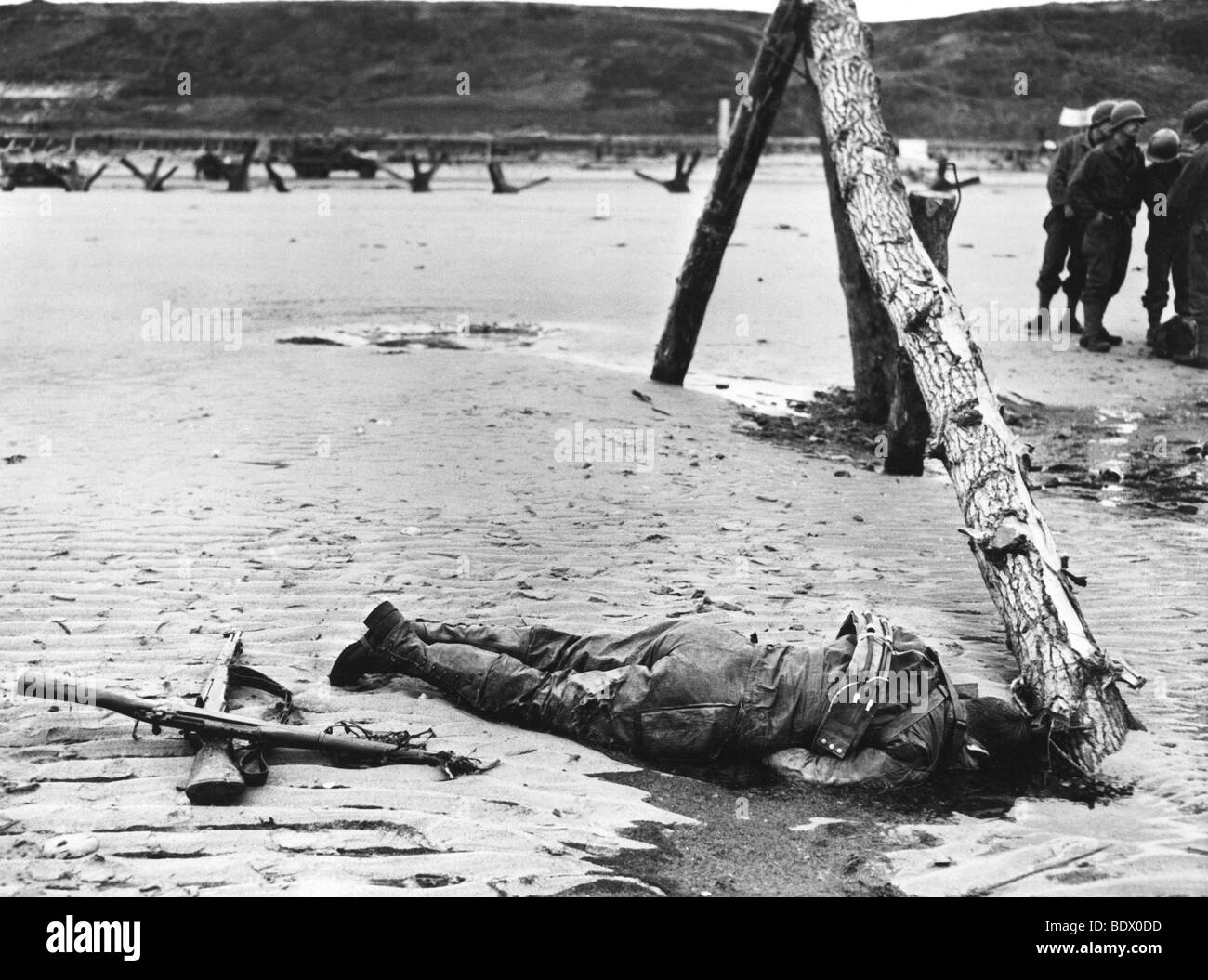 6 juin 1944 - Dead soldat américain sur Omaha Beach à marée montante recule exposant les défenses allemandes. Remarque traversé rifles en hommage. Banque D'Images