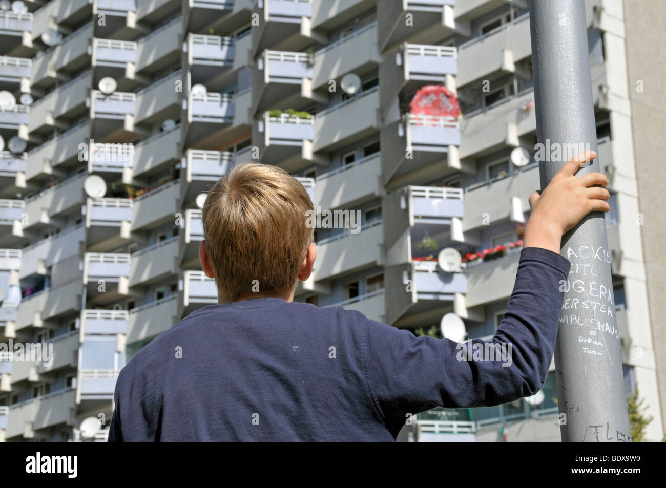 Garçon debout en face d'une tour d'habitation avec des balcons et des antennes paraboliques, ville satellite de Chorweiler en coopération Banque D'Images