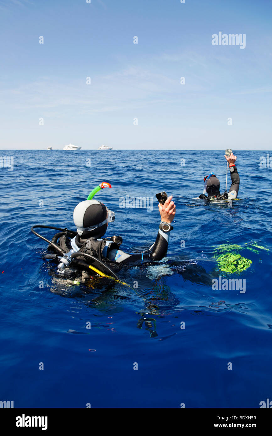 Les plongeurs à la dérive en mer s'efforcent d'obtenir l'attention des gens sur les bateaux de plongée sur l'horizon en clignotant avec des miroirs, l'Égypte, Banque D'Images