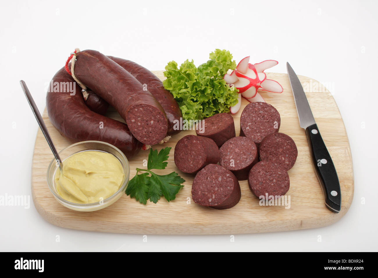 Anneaux de boudin noir, ensemble et couper, garnie avec des radis, moutarde et couteau, sur planche de bois Banque D'Images
