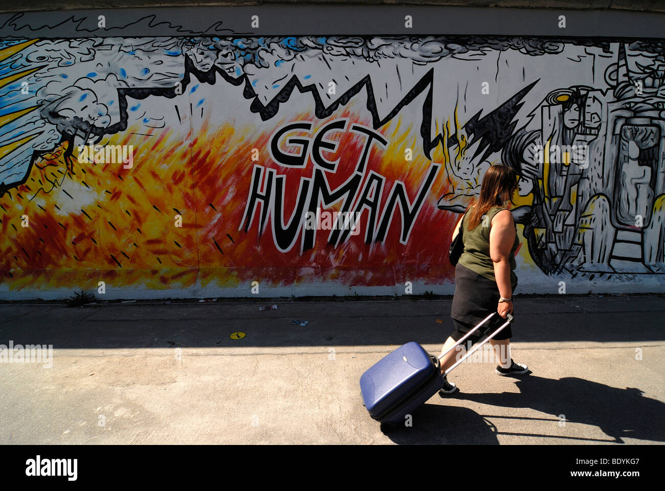 Femme avec une valise roulant passant une œuvre d'art sur le mur de Berlin, l'Eastside Gallery, Graffiti, Berlin, Germany, Europe Banque D'Images