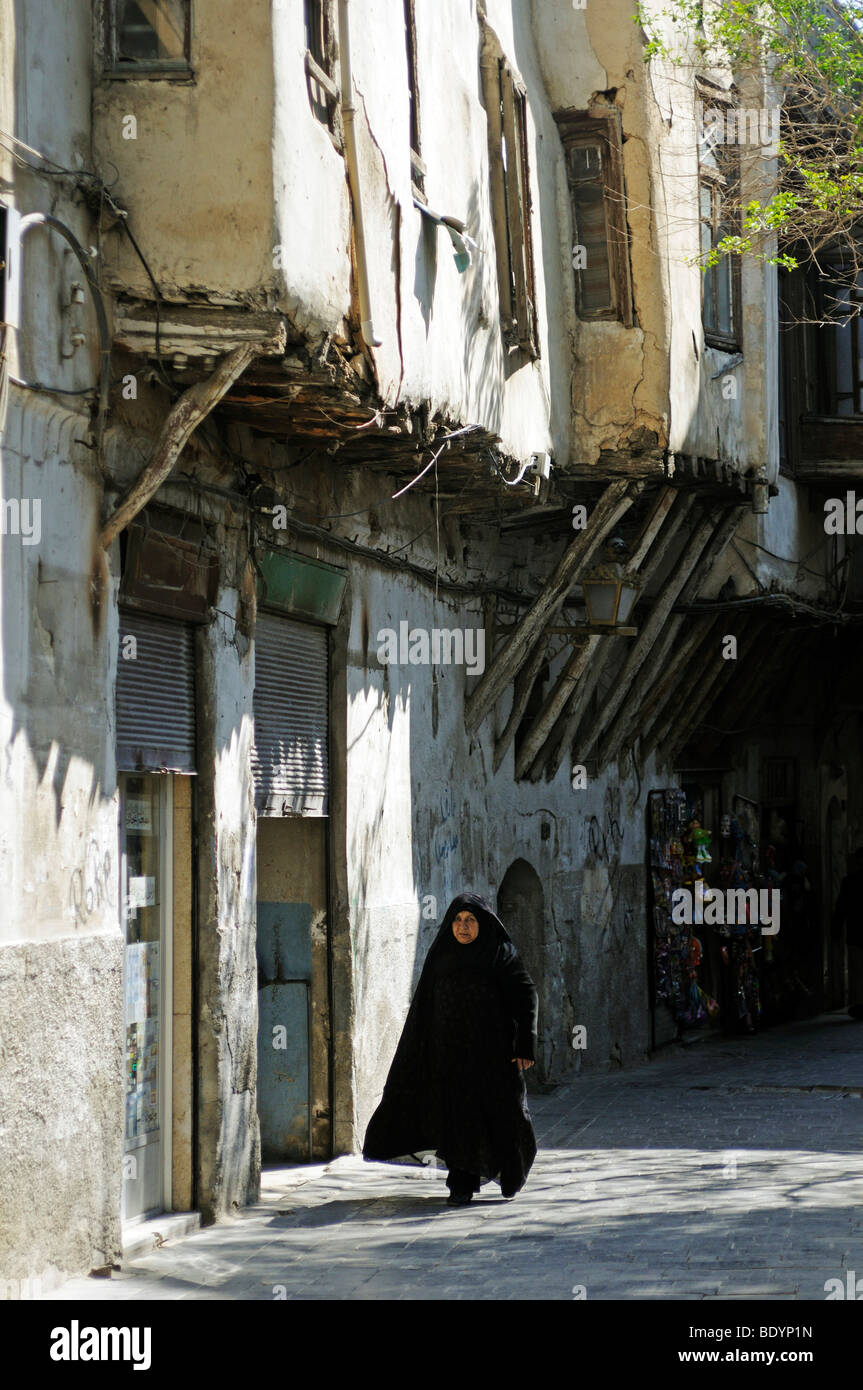 Vieille Femme avec un foulard marcher sous des balcons délabrés, Damas, en Syrie, au Moyen-Orient, en Asie Banque D'Images