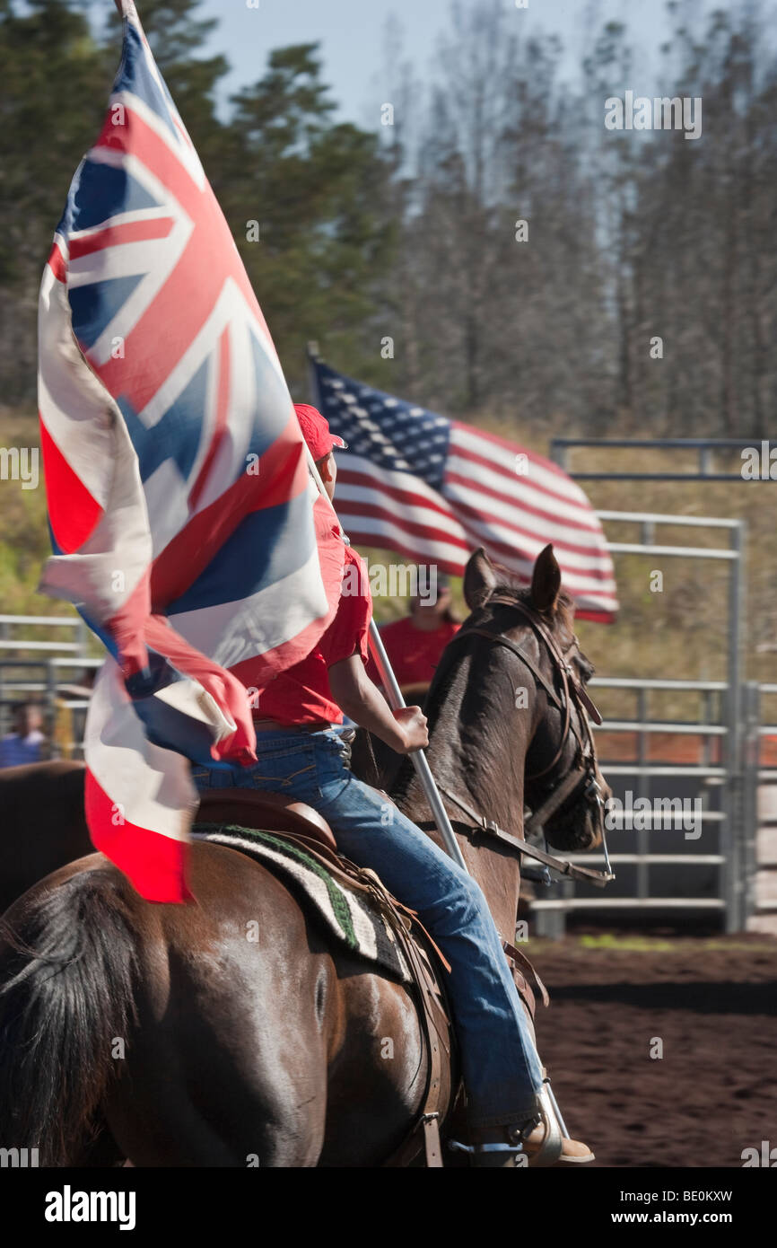 Femme rodeo rider parades Hawaiian flag avec drapeau américain en arrière-plan. Banque D'Images