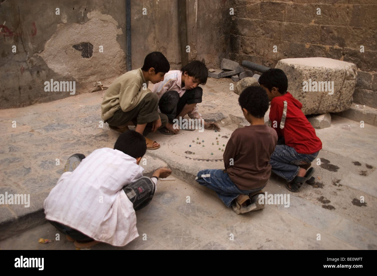 Un groupe de cinq garçons yéménite jouant un jeu de billes dans un cul-de-sac dans les rues du vieux Sanaa, Yémen. Banque D'Images