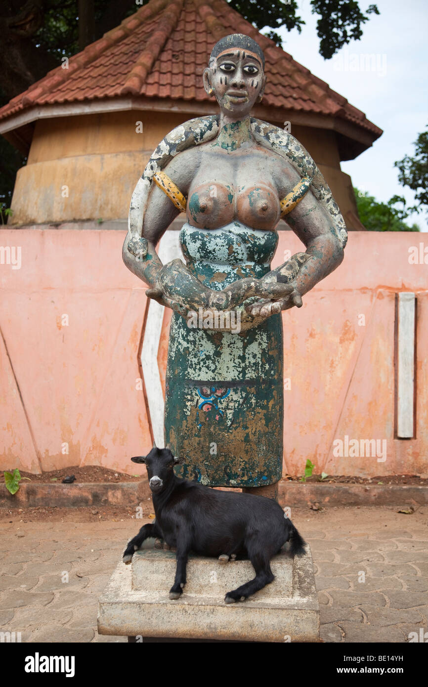En dehors du Temple de pythons dans Oudiah, Bénin, une chèvre se trouve au pied d'une statue d'une femme avec un python. Banque D'Images