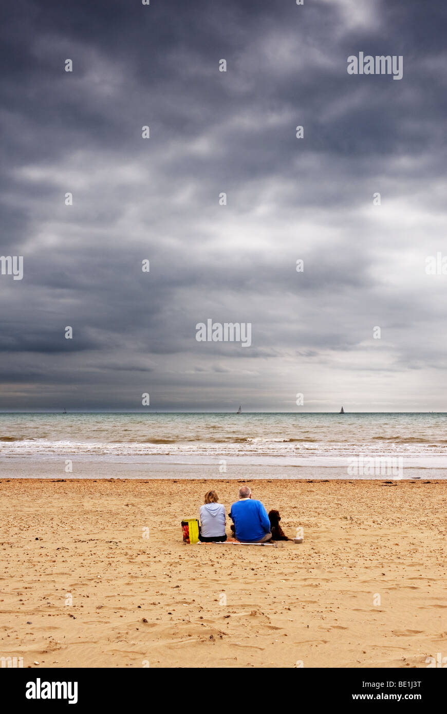 Un couple assis sur la plage sur une journée froide à Camber Sands dans l'East Sussex. Banque D'Images