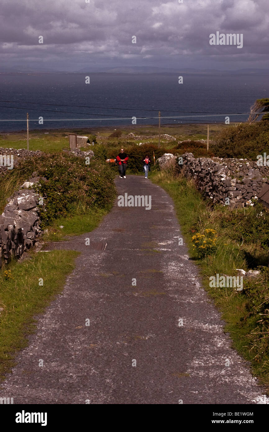 Les touristes marchant sur une petite route de campagne bordée de murs en pierre traditionnels, l'Inis Mor (Inismore) Island, Co Galway, Irlande Banque D'Images