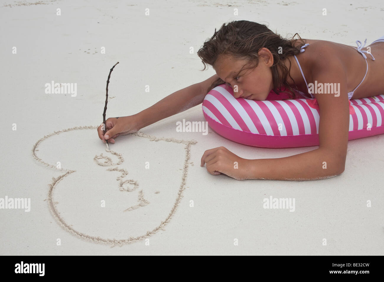 Une fille transi, environ 12 ans, en vacances, est allongé sur un matelas d'air et de peinture d'un cœur avec le mot amour dans le sable Banque D'Images