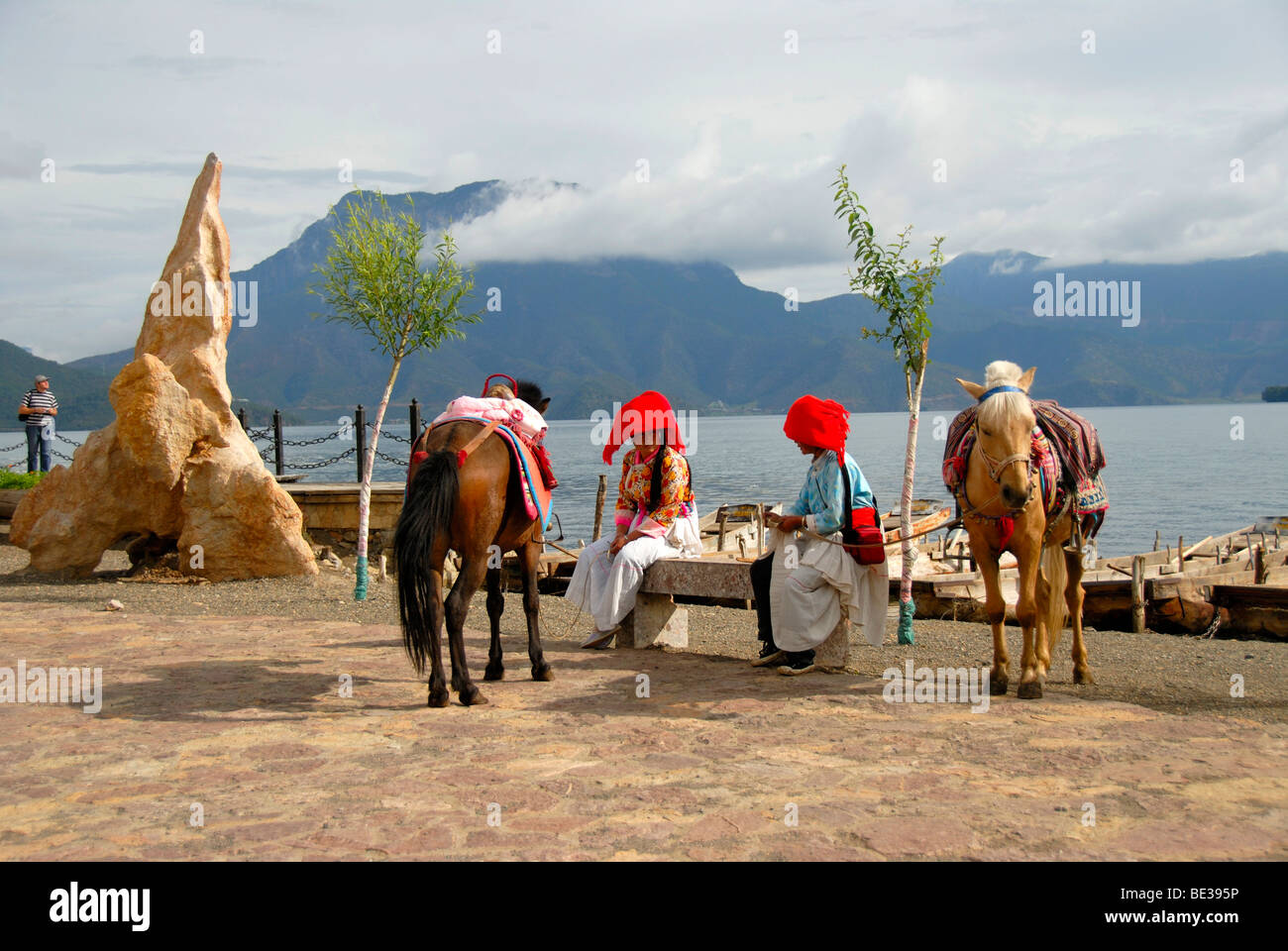 L'ethnologie, les femmes de l'ethnie Mosu habillés en costumes traditionnels avec les chevaux sur la rive, Luoshui, lac Lugu Hu Banque D'Images