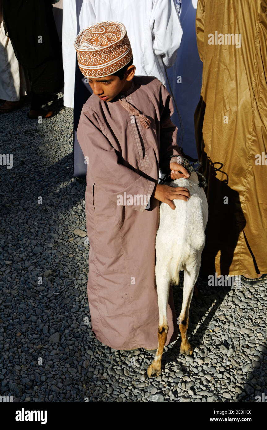 Garçon omanais en costume traditionnel au chèvre, de l'élevage des animaux ou marché à Nizwa, Hajar al Gharbi, Montagnes, région Dakhliyah Al Banque D'Images