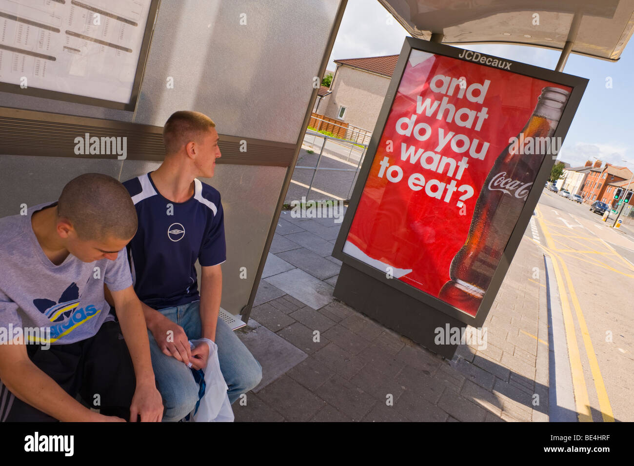 JCDecaux billboard pour Coca Cola sur abri bus avec deux jeunes hommes assis en attente UK Banque D'Images