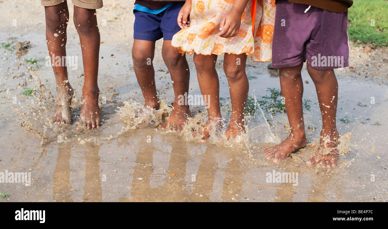 Les enfants indiens de sauter et de s'éclabousser dans une flaque d'eau dans la campagne indienne. L'Andhra Pradesh, Inde Banque D'Images