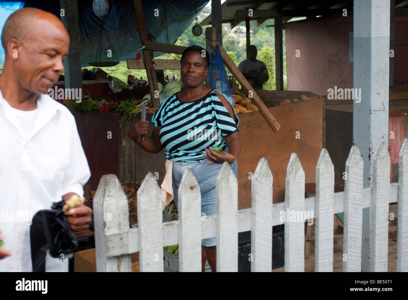 Jamaican homme laisse un marché avec un morceau de gingembre, en tant que femme les regarde. Banque D'Images