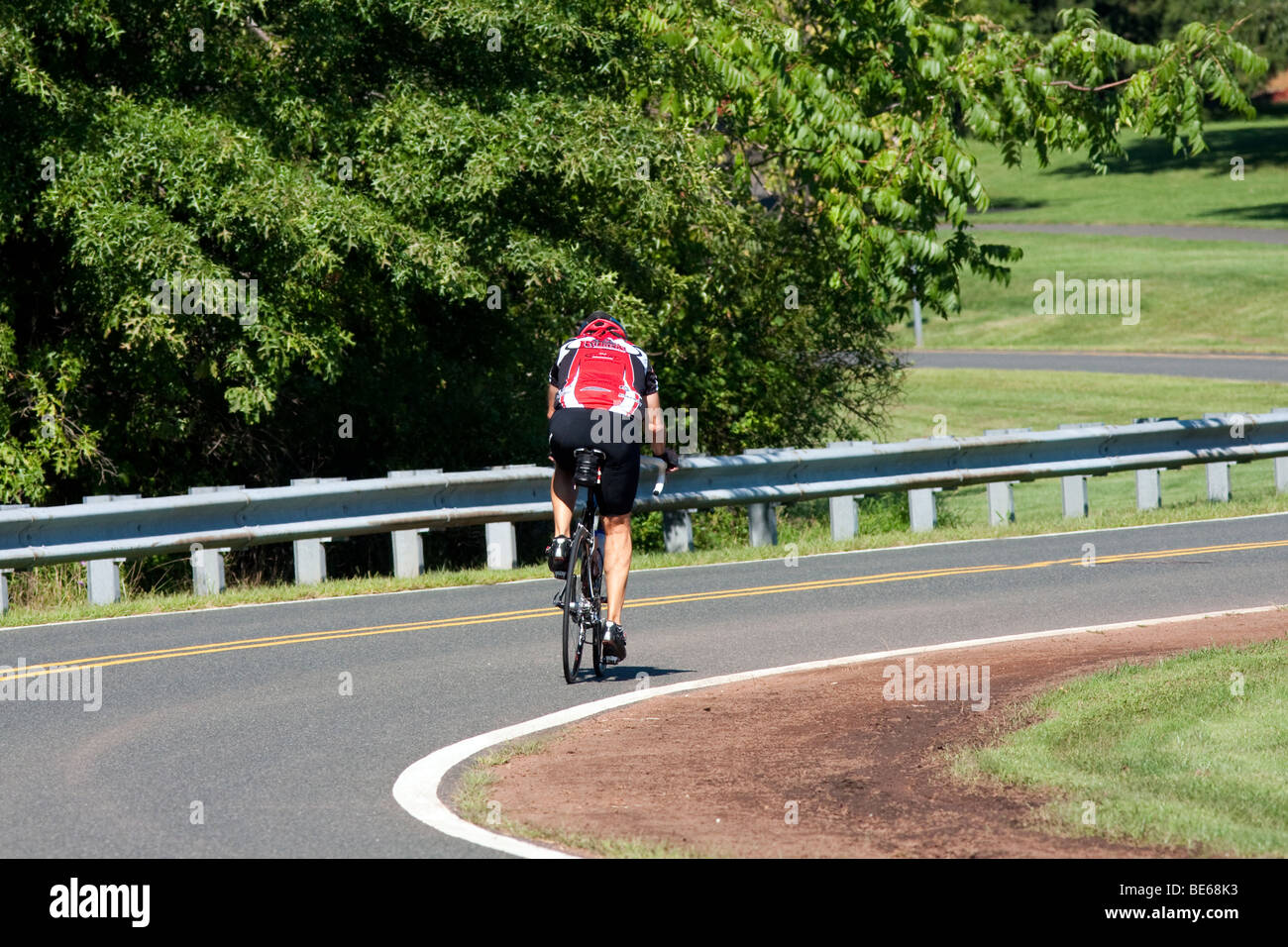 Un homme bicycle rider équitation sur la route portant des couleurs Les couleurs de l'Université Rutgers. Banque D'Images
