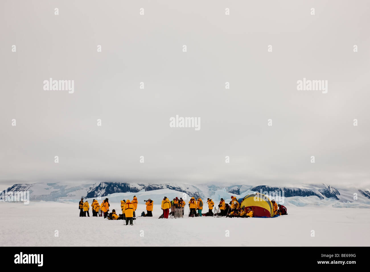 Groupe de touristes eco de l'Antarctique se rassembleront sur la neige près de montagnes couvertes de neige glaciers portant des parkas jaune vif et jaune tente survuval Banque D'Images