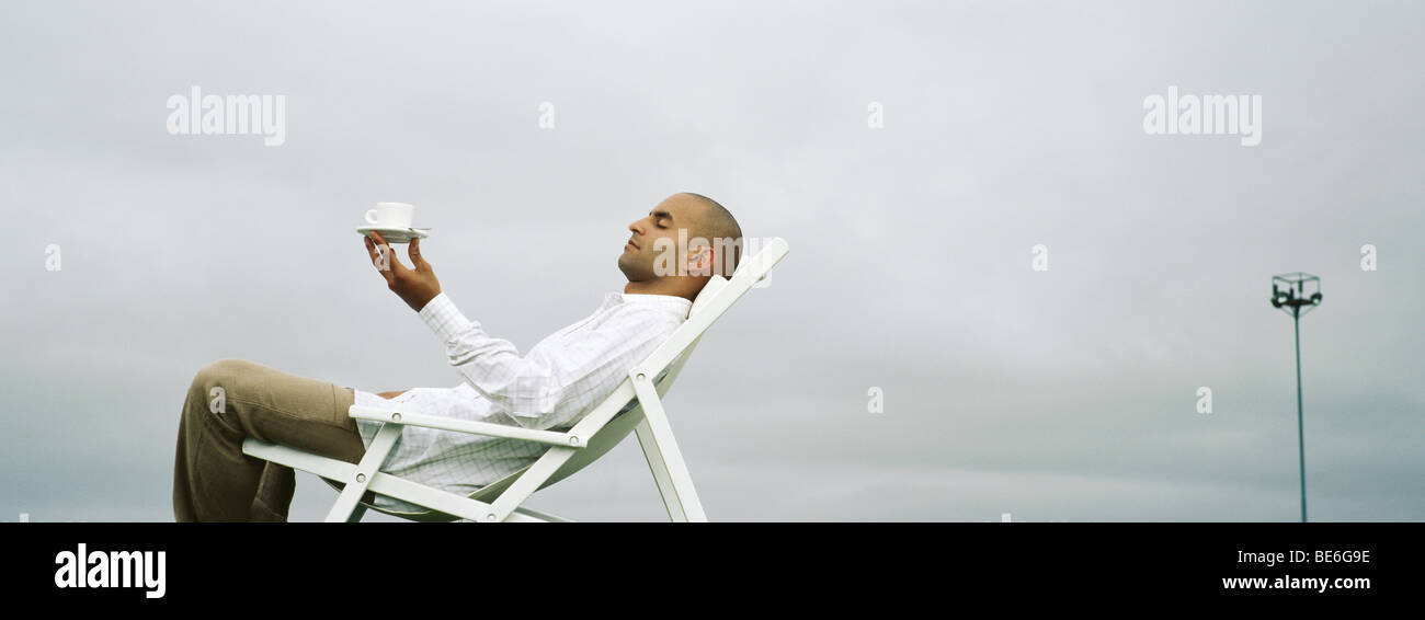 Man relaxing in transat, holding up Coffee cup Banque D'Images